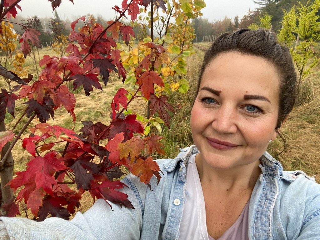 Image of City Councilor Tabatha White taking a selfie in a field with a tree with red fall foliage.